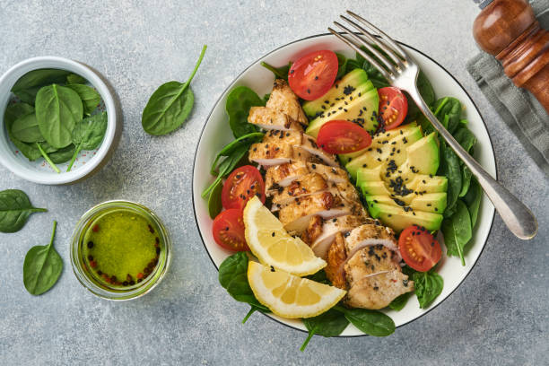 insalata verde fresca con filetto di pollo alla griglia, spinaci, pomodori, avocado, semi di limone e sesamo nero con olio d'oliva in ciotola bianca su sfondo ardesia chiaro. concetto di dieta. spazio di copia in alto - light meal foto e immagini stock