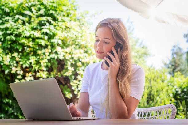 istock Confident young woman talking with somebody on mobile phone and using laptop while sitting outdoors 1333371133