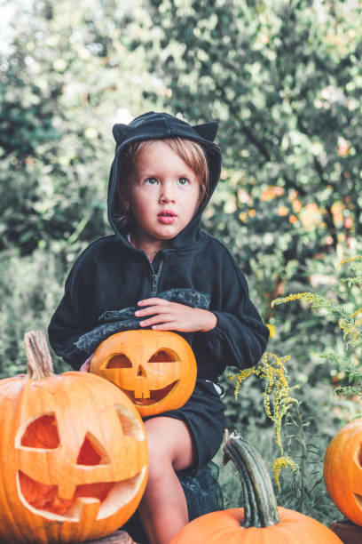 istock Child dressed in black with jack-o-lantern in hand, trick or treat. 1333378564