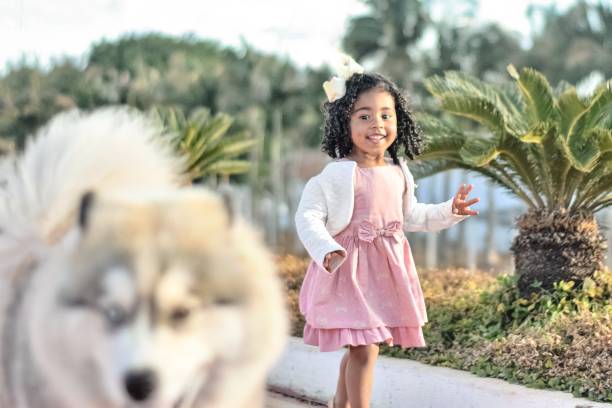 Portrait of a happy little girl walking with her pet, a Siberian husky, at a park. She is smiling as she sees her dog walking in front of her.