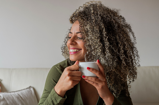 Latin woman from Bogotá Colombia between 40 and 49 years old, sitting on the sofa in her living room, enjoying her coffee on a very bright morning