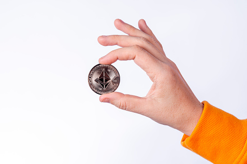 Woman holding physical Ethereum coin (ETH). Cryptocurrency concepts on white background.