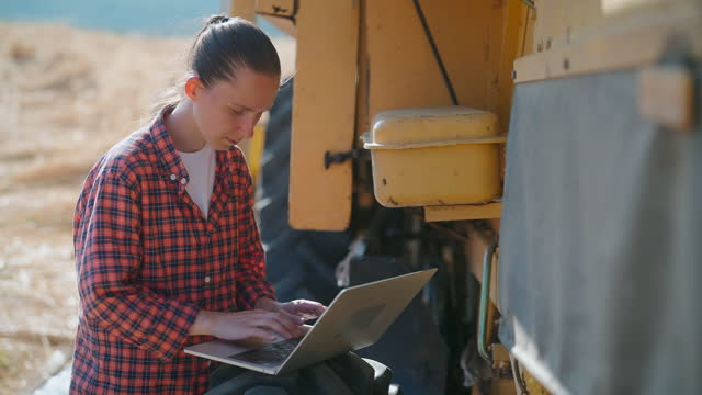 Female farmer using laptop next to combine harvester machine