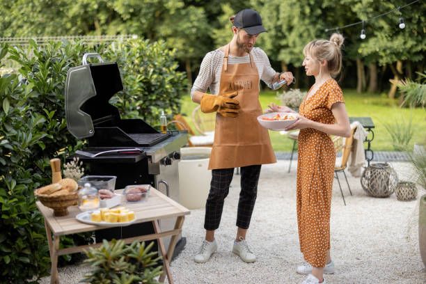 Young couple have fun while cooking vegetables on grill at backyard on nature. Eating and spending summertime at garden of country house