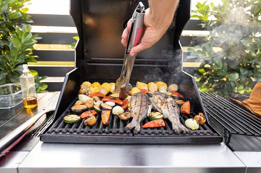 People grilling fish and corn on a modern grill outdoors at sunet, close-up. Cooking food on the open air