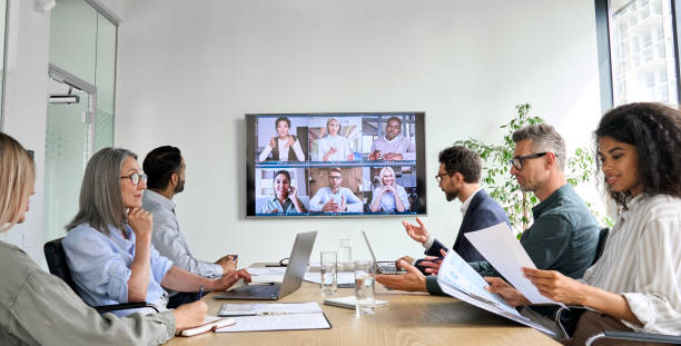 Diverse employees on online conference video call on tv screen in meeting room. Diverse company employees having online business conference video call on tv screen monitor in board meeting room. Videoconference presentation, global virtual group corporate training concept. meeting stock pictures, royalty-free photos & images