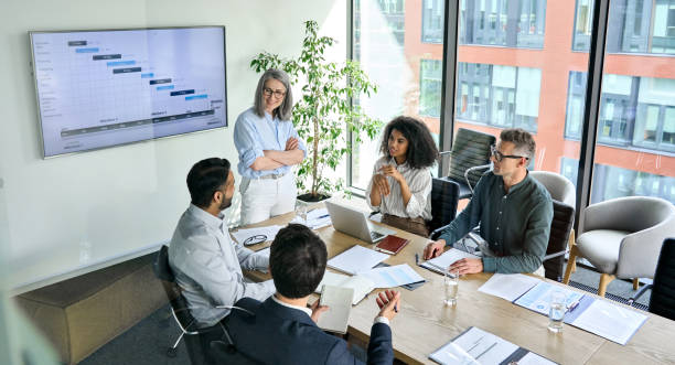 Diverse corporate team working together in modern meeting room office. Senior female ceo and multicultural business people discussing company presentation at boardroom table. Diverse corporate team working together in modern meeting room office. Top view through glass organization stock pictures, royalty-free photos & images