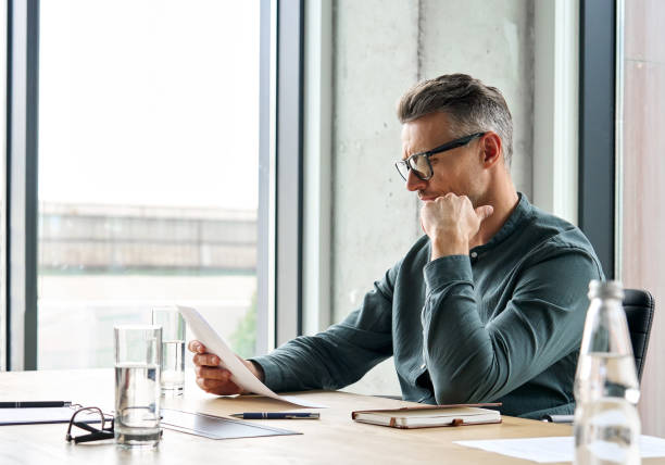 istock Focused mature businessman lawyer reading document sitting at office table. 1333391575