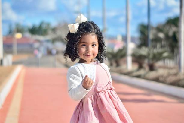 Portrait of a little girl at a park Portrait of a cute little girl hanging out at a park, wearing a pink dress and a white blouse, joyfully enjoying the moment. She is holding some small object and showing it to the camera with a beautiful look on her face. little black girl hairstyle stock pictures, royalty-free photos & images