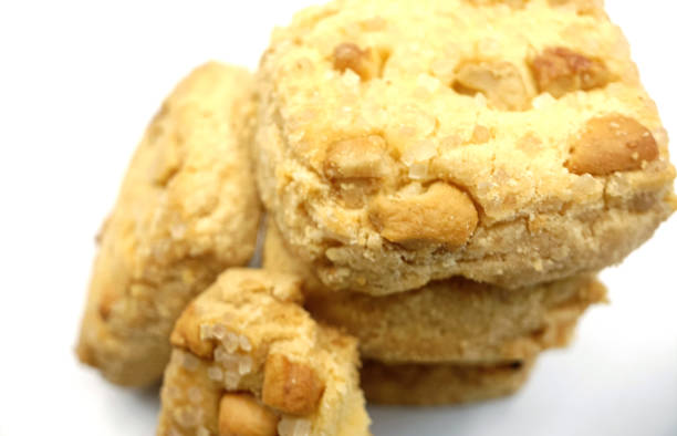 Golden-brown cookies piled together, adorned with crunchy nut toppings, laid artfully on a rustic wooden table. Their inviting aroma promises a delightful treat for any sweet tooth.