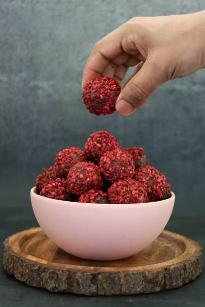 Image of unrecognisable person selecting an individual chocolate from pile in pink bowl on a wooden board, homemade, truffle sweets with ganache centre, luxury chocolate balls coated in dehydrated raspberry pieces, dark grey background, focus on foregroun Stock photo showing a display of homemade, individual, luxury chocolate truffles with a ganache centre and coated in dehydrated raspberry pieces. These luxury chocolate balls are ideal as a birthday present. chocolate fingers stock pictures, royalty-free photos & images