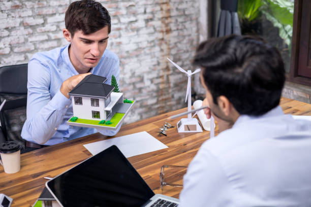 istock Caucasian white Engineer and Architect are discussion ideas working on an architectural design renewable energy on wind turbine and house models in office. 1333396733