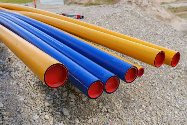 Construction site. Stacks of orange-yellow and blue PVC electrical conduit pipes lies on the gravel..
