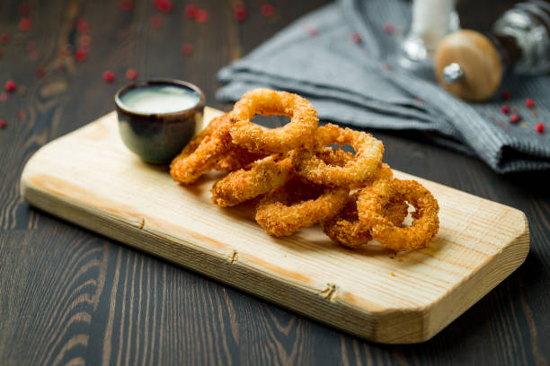 Rings of squid in batter with sauce on board on dark wooden table Rings of squid in batter with sauce on board on dark wooden table calamari stock pictures, royalty-free photos & images