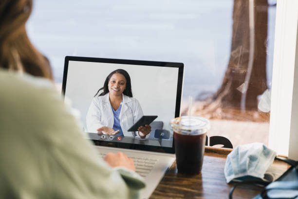 Unrecognizable woman chats with medical colleague on laptop during COVID-19 During the coronavirus epidemic, two female colleagues use video conferencing to meet together.  Both women are in the medical profession. virtual event stock pictures, royalty-free photos & images
