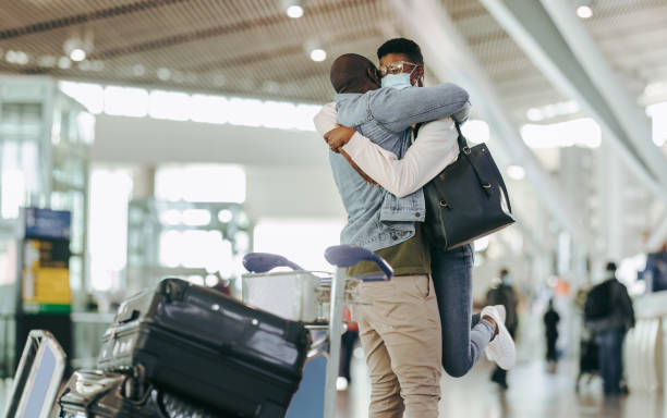 Couple meet after long separation at airport African man hugging and lifting woman at airport terminal. Couple meet after long separation at airport post pandemic lockdown. airport hug stock pictures, royalty-free photos & images