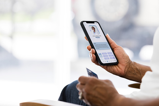 From the comfort of her home, the senior adult woman uses her phone to find a doctor.  She has her credit card ready to pay for the tele-health consultation.