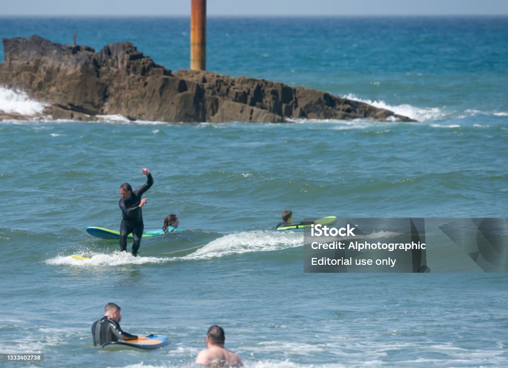Surfing off Bude beach. An accomplished surfer making the most of some small waves off the beach at Bude in Cornwall, England, UK. There are a mix of ages and genders in the water around him. 2021 Stock Photo