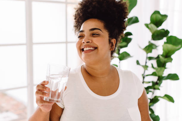 donna sorridente che beve acqua a casa - african descent healthy lifestyle people water foto e immagini stock