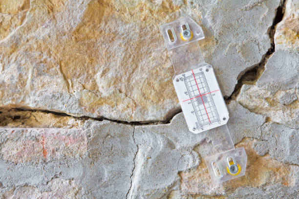 Deep crack in a damaged old stone wall cause due to subsidence of foundations structural failures with plastic mechanical crack meter designed to measure movement across surface cracks and joints grieta profunda en una pared de piedra vieja dañada causa debido a la subsidencia de los cimientos fallas estructurales con medidor de grietas mecánicas de plástico diseñado para medir el movimiento a través de grietas superficiales y juntas
