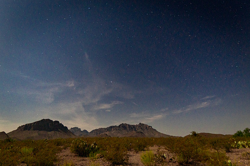 The desert floor is illuminated by moonlight with distant mountains sitting below a sky full of stars.