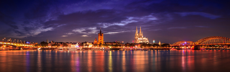 Panorama of Cologne with the Rhine and the illuminated Cologne Cathedral in the background in the evening.