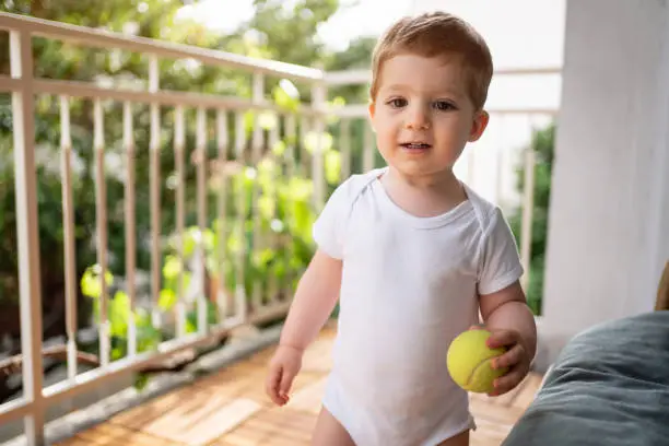 Portrait of a young Caucasian boy with a tennis ball, playing on the 
balcony during a summer day.