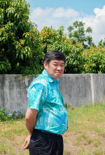 paunchy senior asiatico uomo in piedi e sorridente in giardino d'erba greenfield - paunchy foto e immagini stock