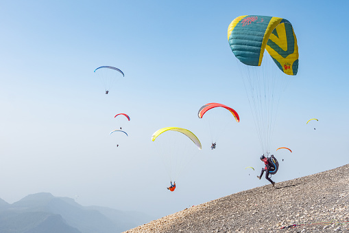 Fethiye, Turkey - october 20, 2018. Paragliders take off from Babadag Mountain in sunny day. Multicolored parachutes in blue sky