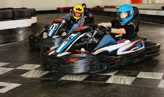 Young man and women competing on racing cars at kart circuit