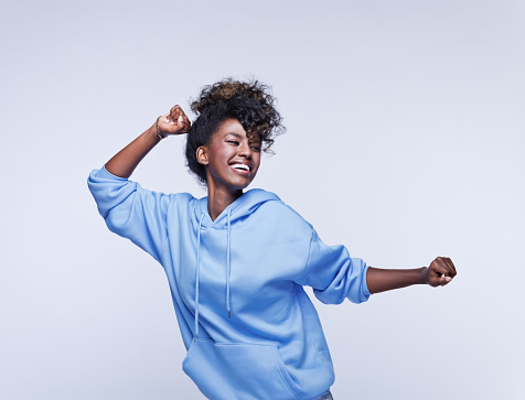 Portrait of happy african young woman wearing blue hoodie. Studio shot on grey background.