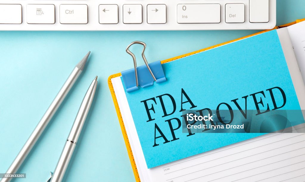 FDA APPROVED text on sticker on the blue background with pen and keyboard FDA APPROVED text on sticker on blue background with pen and keyboard Food and Drug Administration Stock Photo