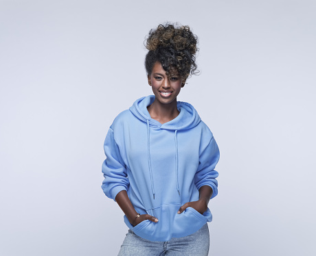 Portrait of confident african young woman wearing blue hoodie, smiling at camera. Studio shot on grey background.