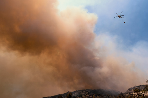 A firefighting helicopter flying through smoke and carrying water to Manavgat forest fire in Antalya, Turkey.
