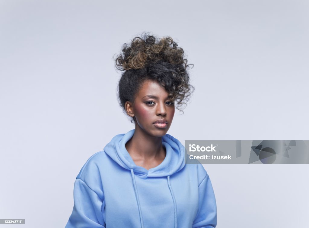 Worried young woman in blue hoodie Headshot of thoughtful african young woman wearing blue hoodie, looking at camera. Studio portrait on grey background. Displeased Stock Photo