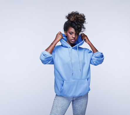 Portrait of confident african young woman wearing blue hoodie, looking at camera. Studio portrait on grey background.