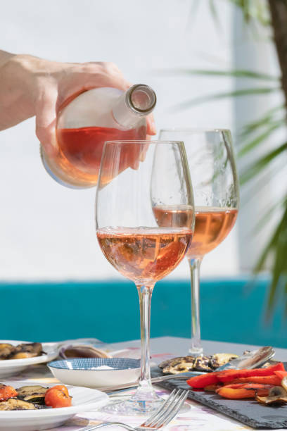 a hand of woman pouring delicious rose wine close up of a hand of woman pouring delicious rose wine from bottle into glass outdoors . lifestyle concept rosé wine stock pictures, royalty-free photos & images