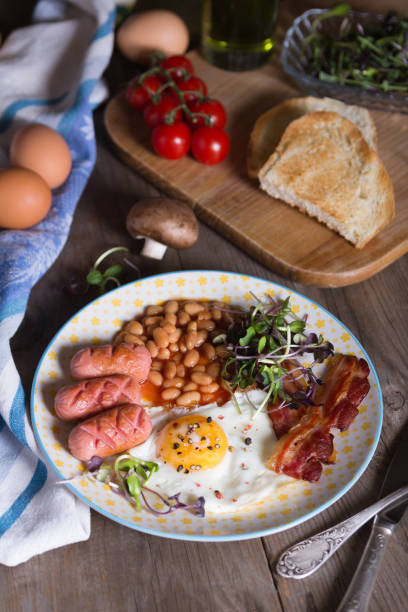 istock Fried eggs with bacon, sausages and beans in tomato sauce 1333445877