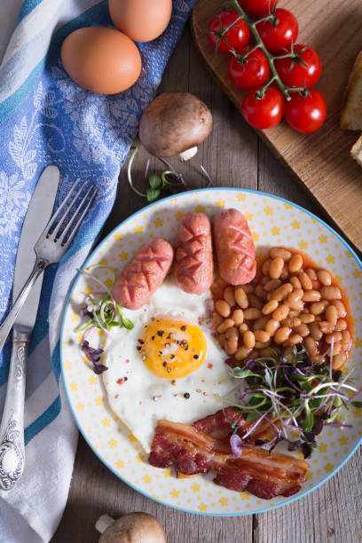 istock Fried eggs with bacon, sausages and beans in tomato sauce 1333445878