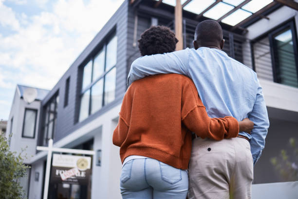 Rearview shot of a young couple standing outside their new home Homeowners in the neighbourhood of their dreams moving house stock pictures, royalty-free photos & images