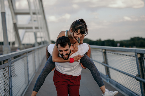 Cheerful athletic couple exercising outdoors on the city bridge, having fun, and living a healthy lifestyle.