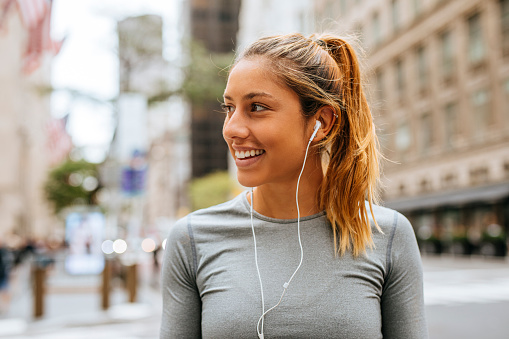 A portrait of a smiling blonde woman listening to music on her smartphone while exercising in New York City