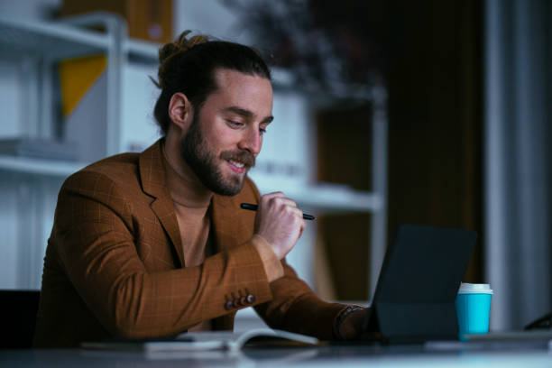 istock Young businessman working late, smiling and looking at something on his tablet 1333458140