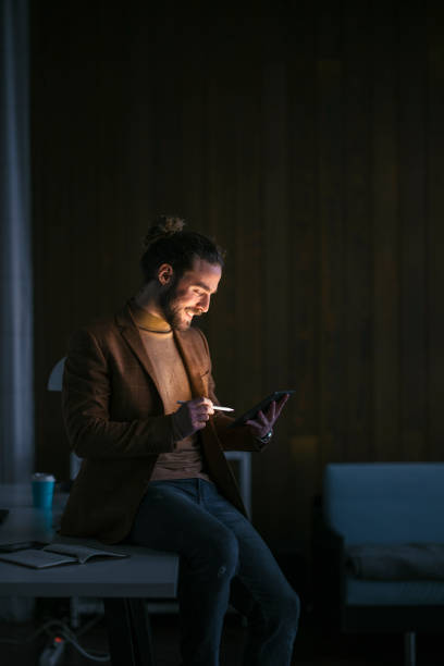 istock Handsome Businessman Sitting on the Desk in His Office Using a Digital Tablet During a Late Night at Work 1333458145