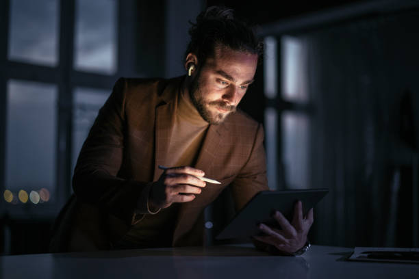 istock Handsome Businessman Wearing Bluetooth Earphones Using a Tablet During a Late Night at Work 1333458159