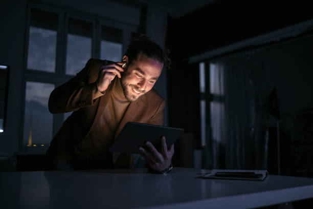 istock Handsome Businessman Wearing Bluetooth Earphones Using a Tablet During a Late Night at Work 1333458164