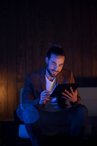 istock Handsome Man Sitting on the Couch Using the Tablet and Looking at the Screen and Smiling 1333458168