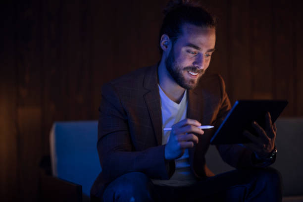 istock Handsome Man Sitting on the Couch Using the Tablet, Looking at the Screen and Smiling 1333458169