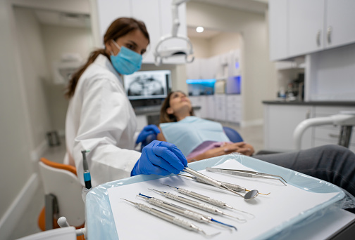 Female dentist using tools while cleaning the teeth of a patient - focus on foreground