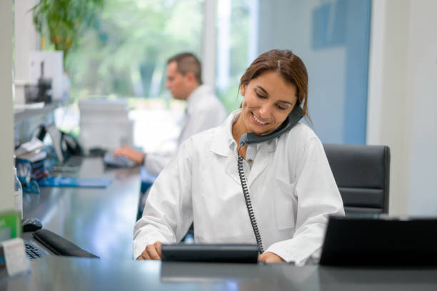 addetto alla reception che lavora in uno studio medico e parla al telefono - dentist dentist office female doctor foto e immagini stock